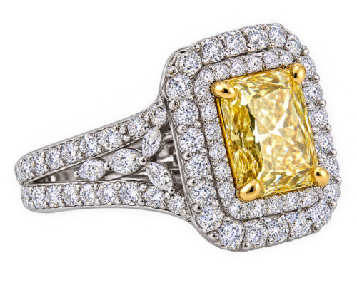 Radiating warmth and brilliance, this exquisite fancy yellow diamond ring showcases a captivating rectangular-cut yellow diamond set in a luxurious double halo of sparkling white diamonds. The intricate split-shank band features additional diamond accents and elegant marquise-shaped details, creating depth, dimension, and exceptional sparkle. A stunning expression of sophistication and timeless luxury, this distinctive piece is designed to make an unforgettable statement.